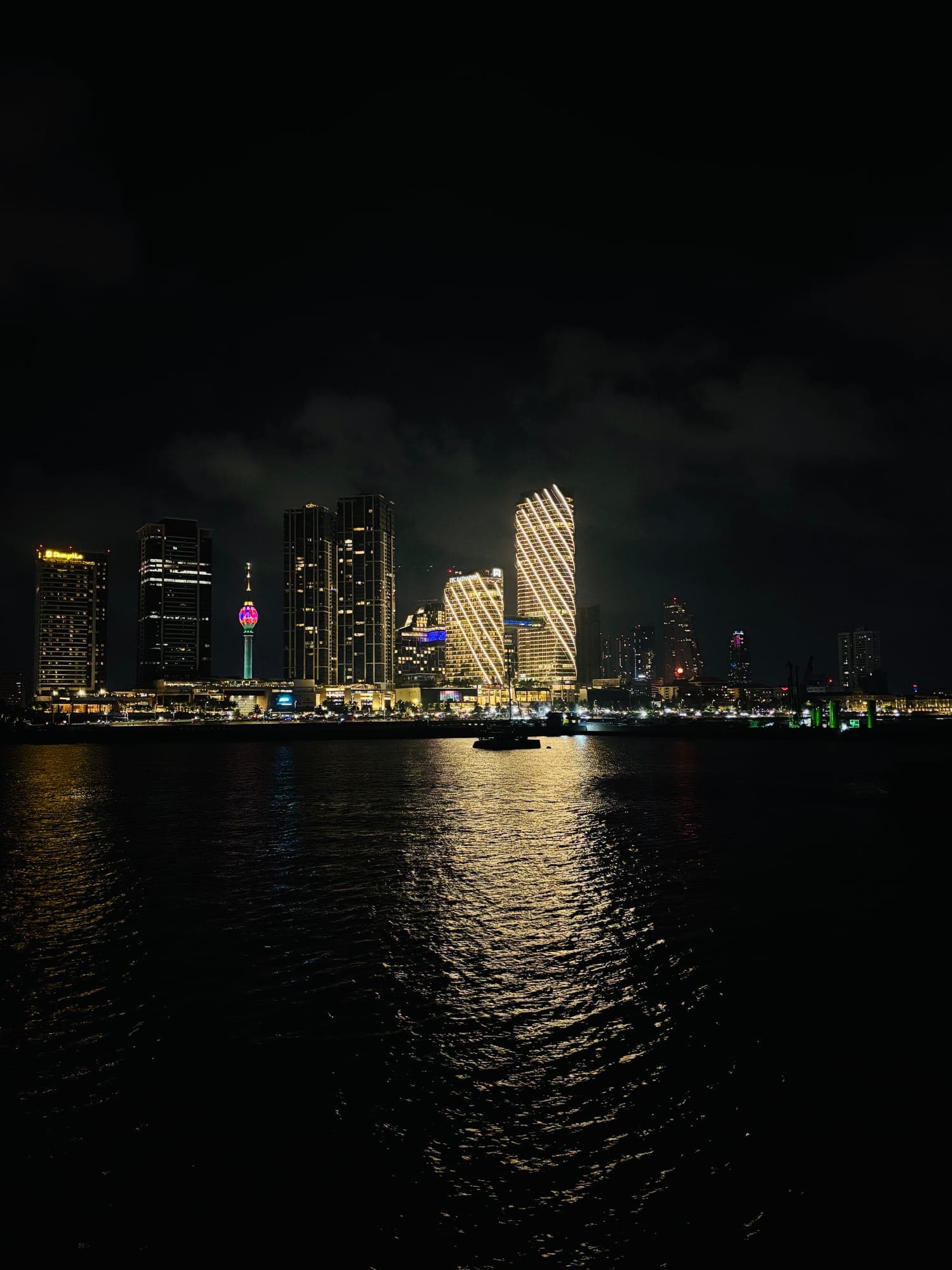 Colombo's skyline at night, with the Lotus Tower and lit high-rises reflected in the water.
