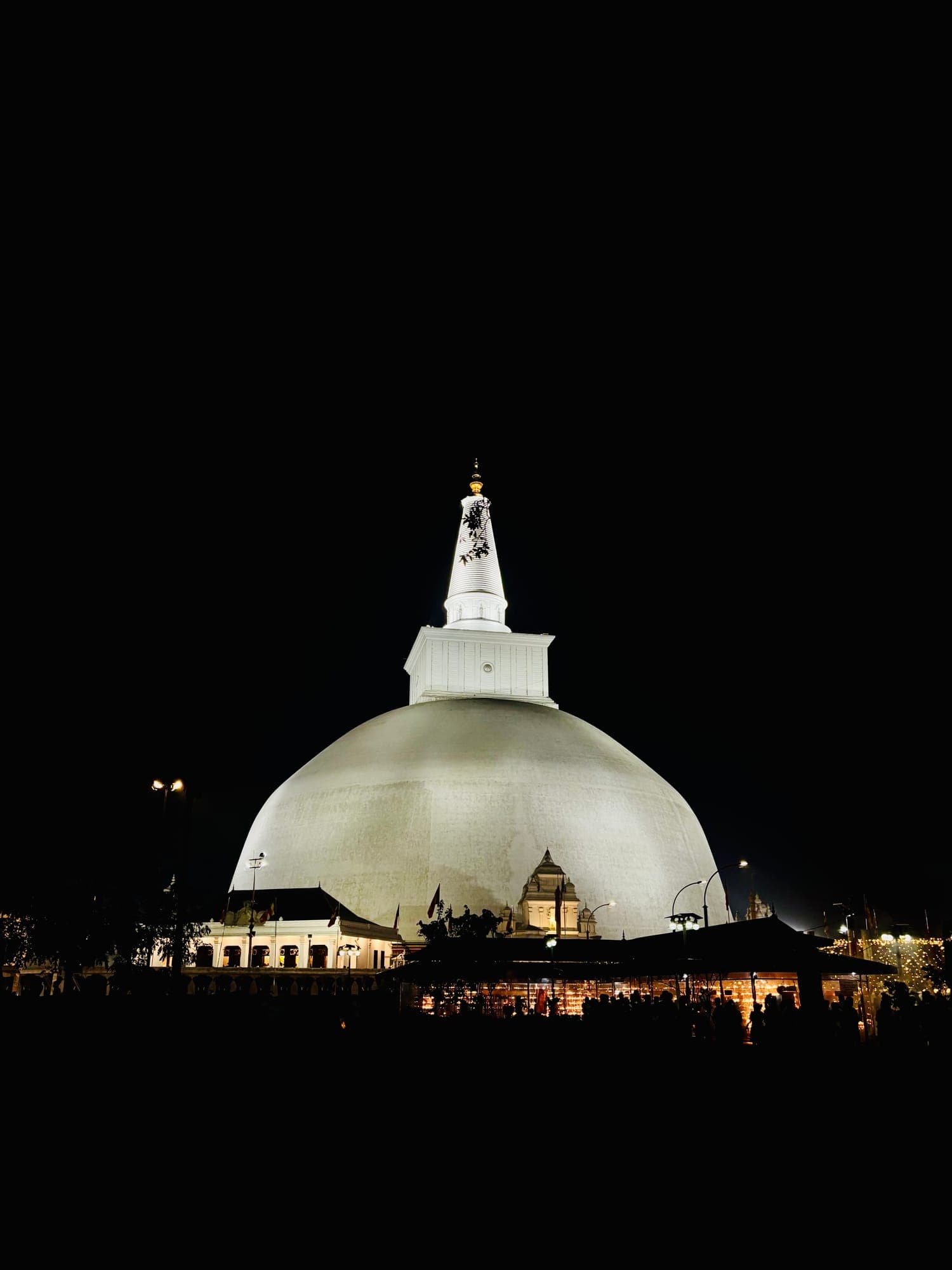 The illuminated white dome and spire of the Ruwanwelisaya stupa against a black night sky.